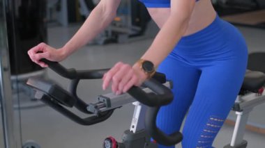 Dikey video. Sportif bir kız koridorda egzersiz bisikletiyle antrenman yapıyor. Yanan kaloriler. Kardiyo eğitimi.