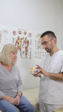 Bir tıp uzmanı sağlık kavramlarını açıklamak için anatomik modeller kullanır. Doktor bir iskelet gösteriyor ve hastalarla omurilik sağlığını tartışıyor, anatominin önemini vurguluyor.