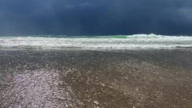 Kumsal sahnesi fırtınalı bir gökyüzü ile çelişiyor, dalgalar sahile çarpıyor. Video bulutlu bir günde güzelliği ön plana çıkarıyor.