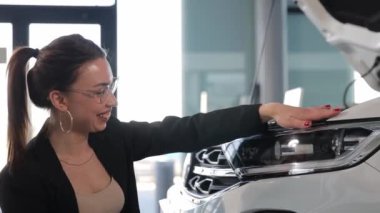 Güzel bayan müşteri galeride açık araba kaputunu inceliyor. Yüksek kalite 4k görüntü