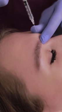 Kadın kırışıklıkları düzeltmek ve cildinin görünümünü iyileştirmek için alnına botoks yaptırıyor. Dikey video