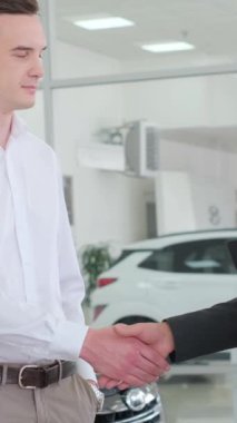 Elbise gömlekli bir adam bir kadın ve bir adamla galeride arabaları tartışıyor. Onlar bir araba galerisinden yeni bir araba alırken gülümsüyorlar. Dikey video
