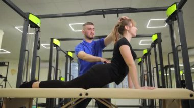 Bir fitness eğitmeni, spor masasında bacakları esnemiş bir kadın müşteriye esneklik ve egzersiz alışkanlıklarını geliştirmek için takım çalışmalarını sergilemesinde yardımcı olur.