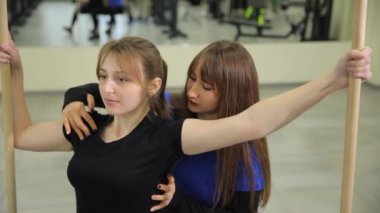 Hareketli bir spor salonunda, genç kadınlar antrenman yapmak için sırıkları kullanırlar. Video, antrenmanlarda takım çalışması ve motivasyonu vurguluyor