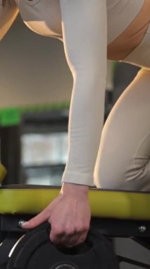 Bir kadın spor salonunda halter kaldırarak, kalçasına, dizine, koluna, göğsüne ve spor takımlarındaki gövde kaslarına odaklanarak antrenman yapmaktır. Dikey video