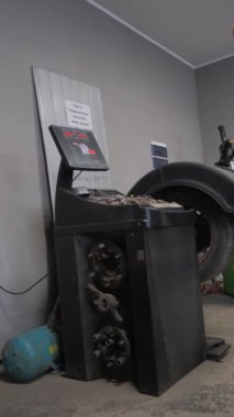Bir kişi bir odada lastik dengeleme makinesinin yanında, araçlar için otomobil lastikleri hazırlıyor. Makine otomotiv dış ekran cihazları olan bir binada. Dikey video