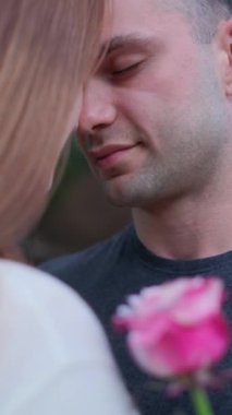 Siyah tişörtlü bir adam pembe gül tutan bir kıza bakıyor. Tarih