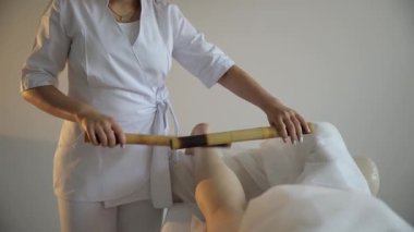 Genç bir kadın rehabilitasyon merkezinin yakın çekimi bambu çubuklarıyla bacaklara masaj yapıyor. Spa tedavisi kavramı. Yüksek kalite 4k görüntü
