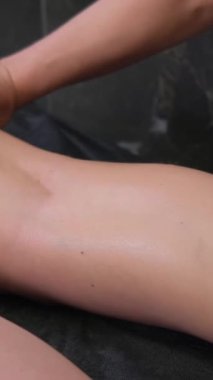 Kanepede sakince yatan genç bir kadının bacaklarına masaj yapan bir elin yakın çekimi. Rahatlatıcı ve canlandırıcı vücut masajı. Spa prosedürleri. Dikey video