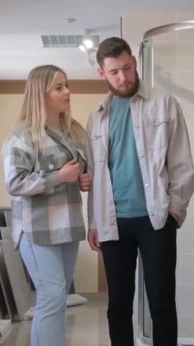 Bir adam ve bir kadın banyodaki bir galeride geziniyorlar, evleri için farklı fayanslara hayran kalıyorlar. Döşeme ve tavan seçeneklerini tartışıyorlar. Dikey video