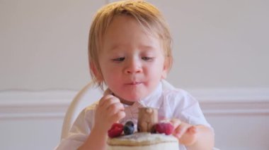 Bir bebek ve küçük bir çocuğun doğum gününü kutlarken yüksek sandalyelerde oturup meyveli pastanın tadını çıkardıkları yürek ısıtan bir video. Çocuk bir mum söndürür, neşeli atmosfere neşe katar.