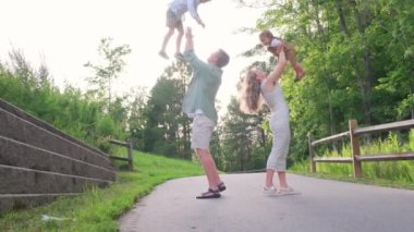 Resimli bir parkta neşeli bir aile gezisi, ebeveynler ve çocuklar arasındaki bağın altını çiziyor, kahkahalar ve eğlenceli aktivitelerle dolu.