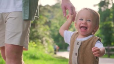 Canlı bir parkta, bir baba ve oğul bir anı paylaşıyor, çocuklar neşe içinde gülüyorlar. Baba, aile bağlarını sembolize eden bir bebek elini tutuyor.