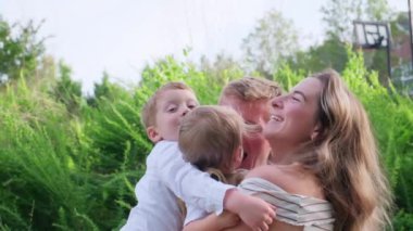 Canlı bir parkta, bir aile güzel anları yakalar. Neşeli bir anne üç çocuğunu kucaklıyor, kahkahalar havayı dolduruyor, sevgilerini gösteriyor.