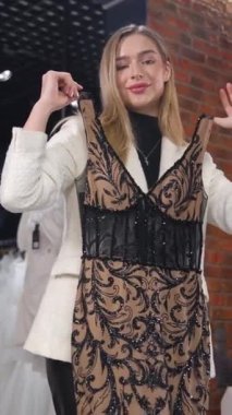 Çekici, narin sarışın gelinliğini gelinlik butiğinde seçiyor. Parti, düğün, doğum günü için gece kıyafeti seçimi. Dikey video