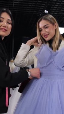 Dikey video satış danışmanı ve genç bir kadın kuaförde bir gece elbisesi seçiyorlar. Gelinin bir arkadaşı için elbise seçiyorum. Gelinlik salonunda güzel kızlar