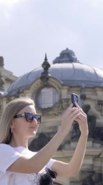 Bir kadın akıllı telefonuyla şehrin güzelliğini yakalar çarpıcı bir binayı ve muhteşem bir kubbenin detaylarını fotoğraflar. Dikey video