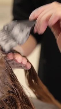 Güzellik salonunda saç boyama. Bir kuaför, fırçayla kadın bir müşterinin saçına boya sürer. Saç boyası. Dikey video
