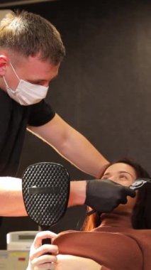 Bir estetik cerrah ve bir asistan modern güzellik kliniğinde genç bir kadını muayene ediyor. Yüzün hatlarını, gözlerinin etrafındaki deriyi inceleyen bir kadın. Operasyonlara karşı. Dikey video