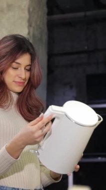 Güzel saçlı dikey videocu kız ev aletleri mağazasında beyaz bir elektrikli su ısıtıcısını inceliyor. Ev için yüksek kaliteli ev aletlerinin dikkatli seçimi.