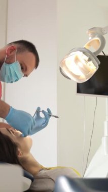 Modern bir diş muayenehanesinde genç bir kadının dişlerini dikey video dişçisi tedavi ediyor. Dişçilerin çalışma süreci.