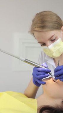 Dikey video dişçisi bir diş kliniğinde bir hastanın dişlerini kontrol ediyor. Tıp, dişçilik konsepti. Diş aletleri hastası, esmer.