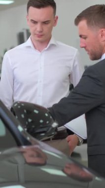 Dikey videoda genç bir satış danışmanı genç bir adama araba alma konusunda tavsiye veriyor. Danışman arabanın içini müşteriye gösterir..