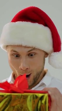 Neşeli bir Noel Baba şapkası takan bir adam güzel paketlenmiş bir Noel hediyesini sevinçle açar ve bu tatil sezonunda hediye vermenin büyüsünü yakalar.