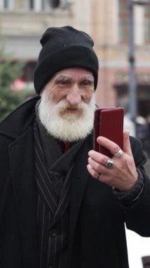 Sakallı yaşlı bir adam teknoloji ile meşgul, neşeyle selfie çekiyor ve nesilleri dijital dünyaya bağlıyor.