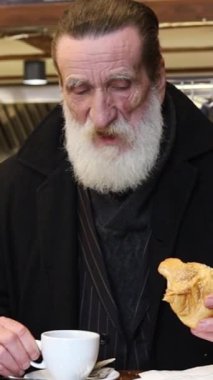 Videoda sakallı bir adamın rahatlatıcı anların tadını çıkarması, sandviç ve kahvenin tadını çıkarması, yemekle rahatlığı ön plana çıkarması yer alıyor.