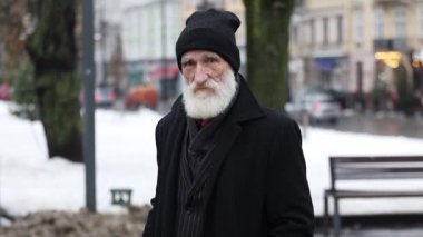Siyah şapkalı yaşlı bir adam, kışın dingin ve yumuşak karları arasında düşünceli bir şekilde duran karlı bir arazide yürüyor.