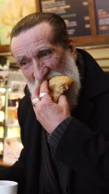 Samimi bir kafe sahnesi, sakallı bir adamın sandviç ve kek gibi çeşitli yiyeceklerin tadını çıkardığını, rahatlatıcı bir atmosferde kahvenin tadını çıkardığını gösteriyor.