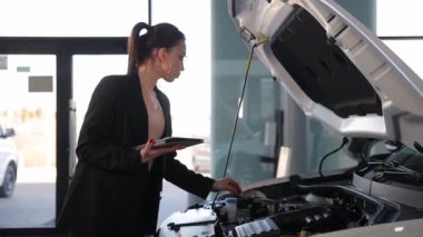 Bir araba galerisinde genç bir bayan yönetici motoru kontrol ediyor ve elinde bir tablet tutuyor. Yüksek kalite 4k görüntü