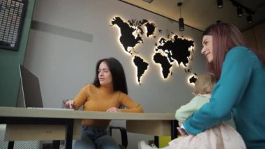 Yürek ısıtan bir videoda, bir kadın bebeğini bir masa başında bir dünya haritasıyla beşikte tutuyor. İki kadın daha sonra neşeli bir anı paylaşıyor, bu da işbirliğini gösteriyor.