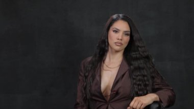 Kahverengi ceketli, uzun siyah saçlı bir esmer bir sandalyede oturuyor. Yüksek kalite 4k görüntü