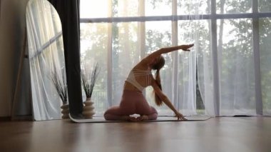 Sakinleştirici bir video, güneşli bir odada yoga yapan bir kadını gösteriyor. Poz verirken, izleyiciler yoganın huzur ve farkındalığını yaşıyorlar.