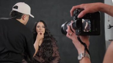 Bir fotoğrafçı, bir makyözün siyah saçlı bir mankenin dudaklarını nasıl boyadığını filme alır. Yüksek kalite 4k görüntü
