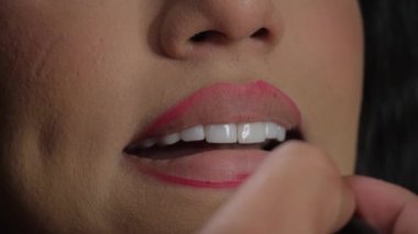 Bu video, dudak makyajı için bir güzellik rutinini vurguluyor, çeşitli ruj gölgelerini fırçayla süren, dudaklarını dönüştüren bir kadın var.