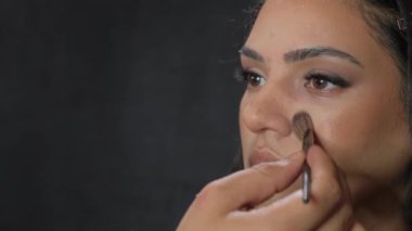 Bu güzellik videosunda bir kadın makyaj sanatçısı özelliklerini gizleyici ile geliştirir, kaşlarını mükemmelleştirir ve göz farı sürer.