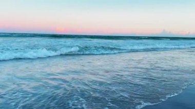 Gün batımında dalgaların kıyıya vurduğu sakin bir kumsalın güzelliğini hissedin. Bu video, barış için ideal altın renkleri sergiliyor.