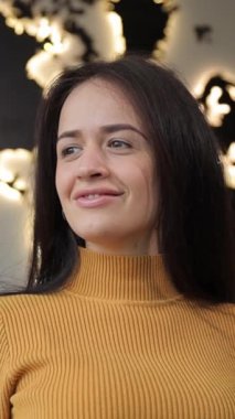 Dikey video, sarı kazaklı genç bir kadın büyük bir dünya haritasının önünde duruyor, gözleri dalgınlıkla kapalı gülümsüyor, merak ve keşif hissini iletiyor.