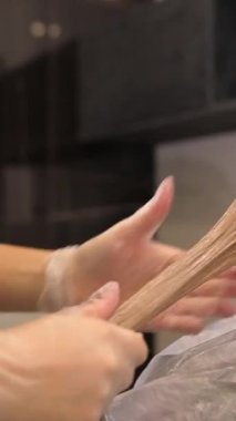 Dikey video, kadın müşteri, bir kuaför renkçisinin sandalyesinde oturuyor ve sarı saçlarını bir güzellik salonuna boyuyor, yakın plan bir portre. Yüksek kalite 4k görüntü