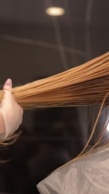 Dikey video, kuaför saçlarını boyadıktan sonra müşterilerinin ıslak saçlarını tarıyor. Yüksek kalite 4k görüntü