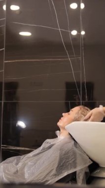 Dikey video, güzel sarışın kadın müşteri profesyonel kadın kuaförüyle güzellik salonunda kuaförlük yapıyor. Yüksek kalite 4k görüntü