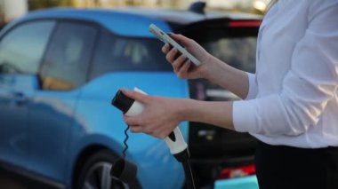 Benzin istasyonundaki mavi araba. Kapalı kadın istasyonda elektrikli arabasını şarj ediyor. Yüksek kalite 4k görüntü