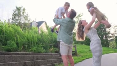 Parkta kaynaşan bir ailenin yürek ısıtan videosu. Ebeveynler çocuklarıyla şakalaşıyorlardı, onları tutuyorlardı ve güzel bir açık hava sahnesinde birlikte gülüyorlardı.