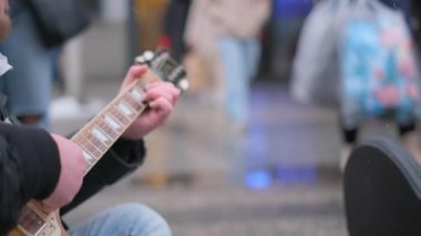 Kalabalık bir sokakta gitar çalan bir sokak müzisyeninin yakın çekimi..