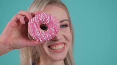 Hevesli bir kadın neşeli pembe bir çöreği gözünün önünde tutuyor ve ifadesine tuhaf bir dokunuş ekliyor.