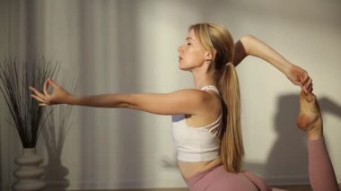 Genç bir Amerikalı sarışın kadın güneş ışığının arka planıyla denge egzersizleri yapıyor. Yoga pozu. Evde meditasyon