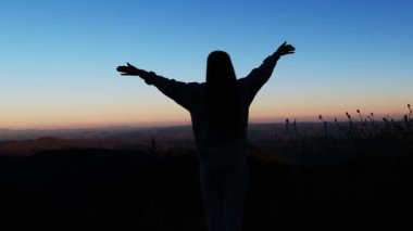 Gün batımında tepede bir kadının çarpıcı görüntüsü, altın renklere karşı silueti özgürlüğü ve doğa bağlantısını simgeliyor.